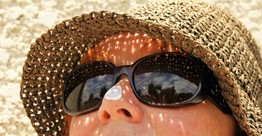 A woman with sunglasses looks up. She has a dab of sunscreen on her nose
