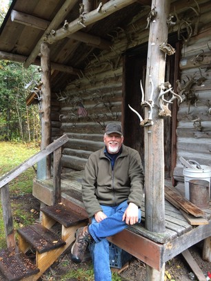 Rick Barta sitting on the deck of his log cabin