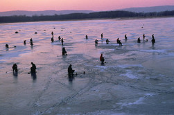 People icefishing on lake at sunset