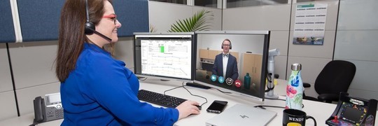 Woman at desk having an online meeting. The other person in the meeting is pictured on her computer screen.