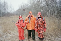 three hunters in blaze orange with a deer stand in the background