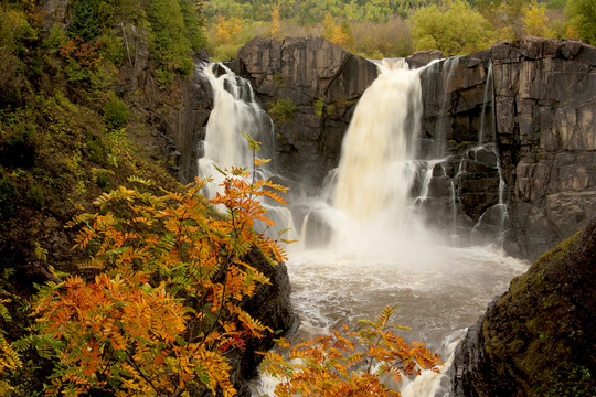 Photo of waterfalls with orange leaves in the foreground