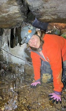 Woman with helmet on all fours smiling at cave entrance