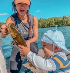 Woman holding a fish and smiling while young child looks in awe.