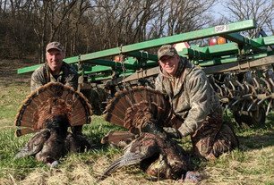 two turkey hunters with birds near farm equipment 