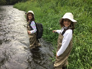 two young anglers, sisters, standing in a trout stream with trout fishing gear