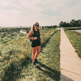 Woman standing by trail with prairie grass and creek in background