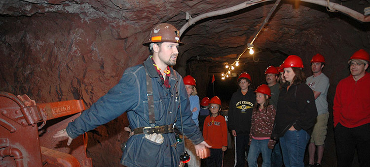 Man showing mining equipment to a group, while underground.