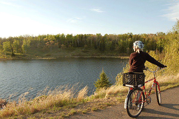 Woman holding bike standing on trail and looking at sunset over a lake