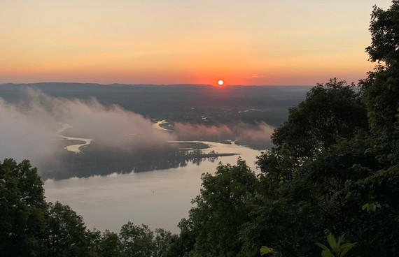 Sunset over a winding river, with bluffs covered in trees and low clouds