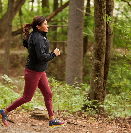 Brown woman running on trail, captured as both feet are off the ground