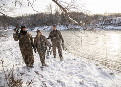 three archery hunters walking along a river and smiling in the winter