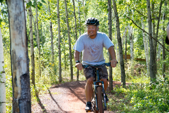 Asian man riding down a mountain biking trail, smiling.