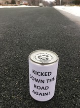 Can in road with sign "Kicked Down the Road Again!"