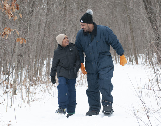 A black boy and his dad walking on snow and smiling at each other with love.