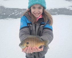 young angler standing on the ice holding a fish she caught while ice fishing
