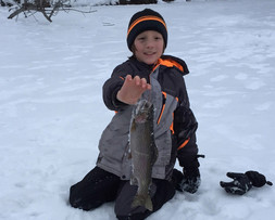 young angler on the ice holding a trout he caught