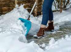 person's legs as they shovel snow from a stone walkway