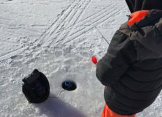 a kid ice fishing and standing by a hole with a fishing pole