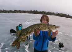 young angler holding a large pike on the ice