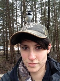 Selfie of a woman with a cap and a chickadee on her head.
