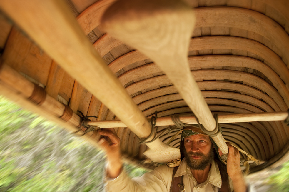 Interior of a wooden canoe, shown upside down on a man's shoulders.