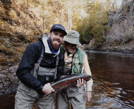 couple anglers holding a trout near stream