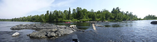 Panoramic photo of St. Louis River, showing a rock, boat and trees in the background.