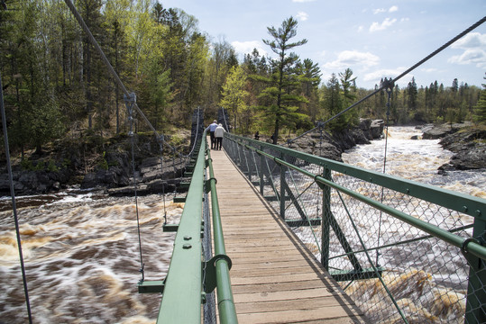 An elderly couple walks across the swinging bridge at Jay Cooke State Park
