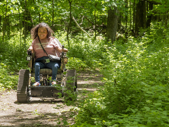 A woman uses an all-terrain track chair through a forest