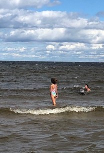Two kids seen from a distance standing and swimming in a large lake with white caps.