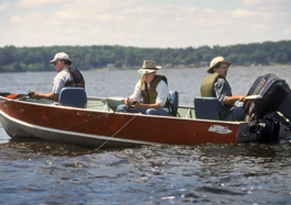 three guys in a fishing boat with life jackets fishing