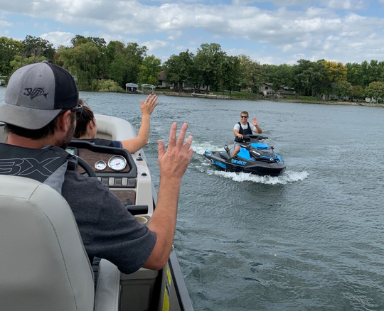 Two people on a boat waving to one person on a jet ski