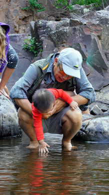 Hmong grandpa holding his young grandson over the water while helping him dip his little hand.