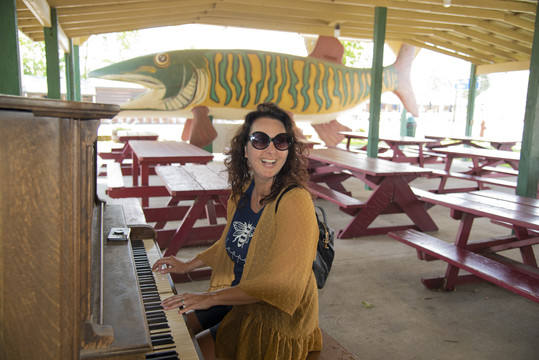 A woman plays the piano in front of a giant statue of a fish