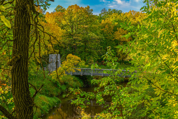 Bright colors, from bright green, yellow and orange foliage to blue skies, partly concealing a historic bridge over the Middle River.