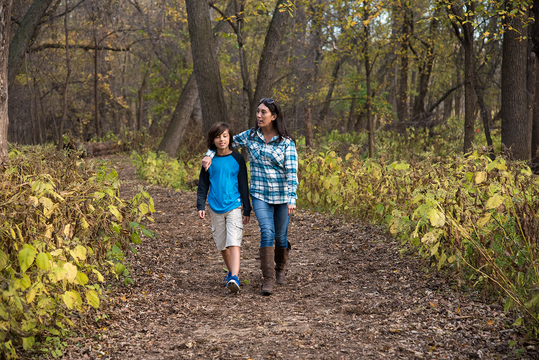 A woman places her arm around her son's shoulders as they hike in the forest