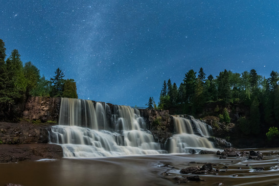 Waterfalls under a starry sky, framed by evergreens.