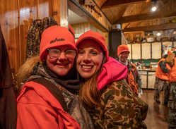 two hunters posing for a photo in deer camp after a hunt and one with her glasses foggy from being outside