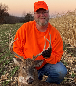 deer hunter with deer he harvested this year, holding antlers near corn field and grass