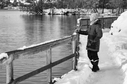 Black and white photo of a woman in a wintry scene, staring at the water