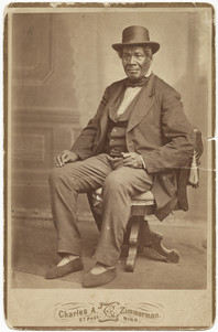 Sepia photo of Black man sitting on a chair, elegantly dressed. 