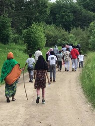 Group of families seen from behind walking down a trail, some women wearing traditional East African clothing.