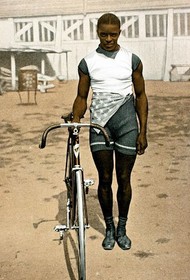 A Black cyclist posing with his bike, looking sharp in his professional racing outfit.
