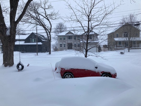 A snow-covered neighborhood, with several inches of snow on top of a red car