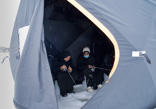 Two girls ice fish in a tent