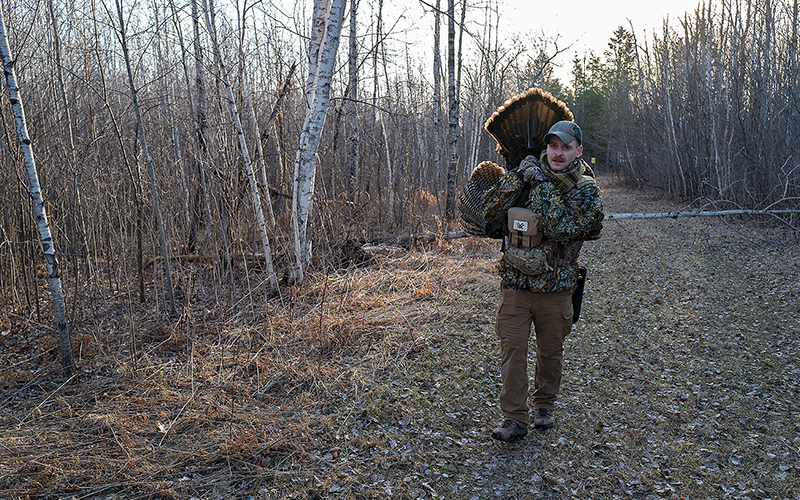 A hunter carrying a wild turkey over his shoulder