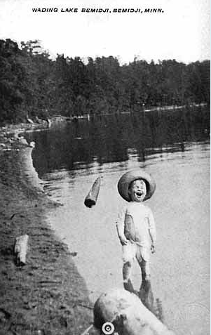 Antique photo of a young child with a hat laughing while wading on Lake Bemidji.