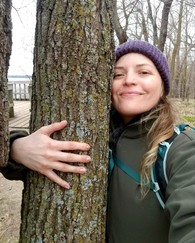 A woman smiling and hugging a tree.