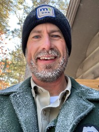 Man in Minnesota state park uniform, with beard and jacket lapels covered in snow.